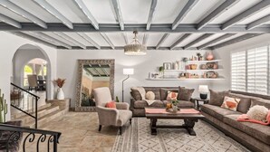 Una sala de estar con sofá, sillón y una mesa de centro, una araña y una estantería con adornos.