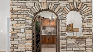 Un arco de piedra que da acceso a una cocina con armarios de madera y encimera de granito.