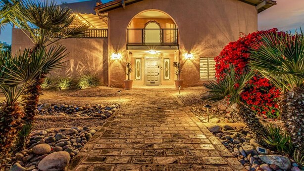 Una casa de estuco con entrada central, un balcón y un jardín bien cuidado con rocas y plantas.