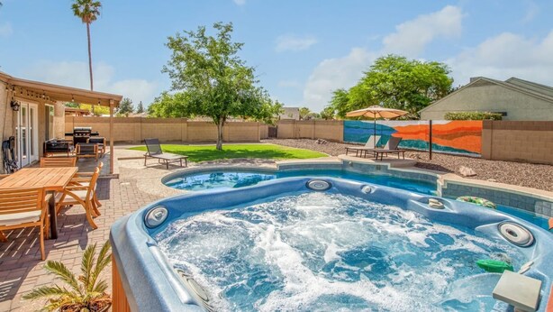 Un jacuzzi rodeado de muebles de madera para terraza, una piscina y un mural en la pared.