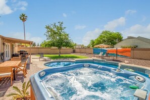 A hot tub surrounded by wooden deck furniture, a swimming pool, and a mural on the wall. - Corbell Park Casa W Pool Spa - S Tempe (Tempe)