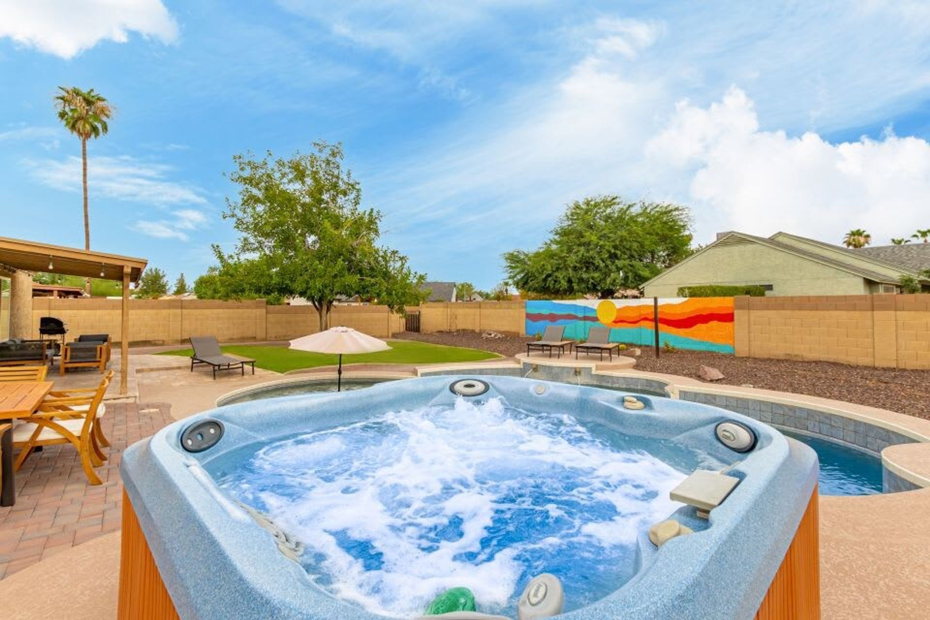Un bain à remous dans un jardin, avec une terrasse, une fresque murale et une piscine.