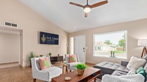Una sala moderna con ventilador de techo, un ventanal con persianas, un sofá, dos sillones, una mesa de centro y un letrero que dice "Old Town Rental".