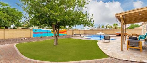 A backyard with a swimming pool, a covered seating area, and a mural on the wall.