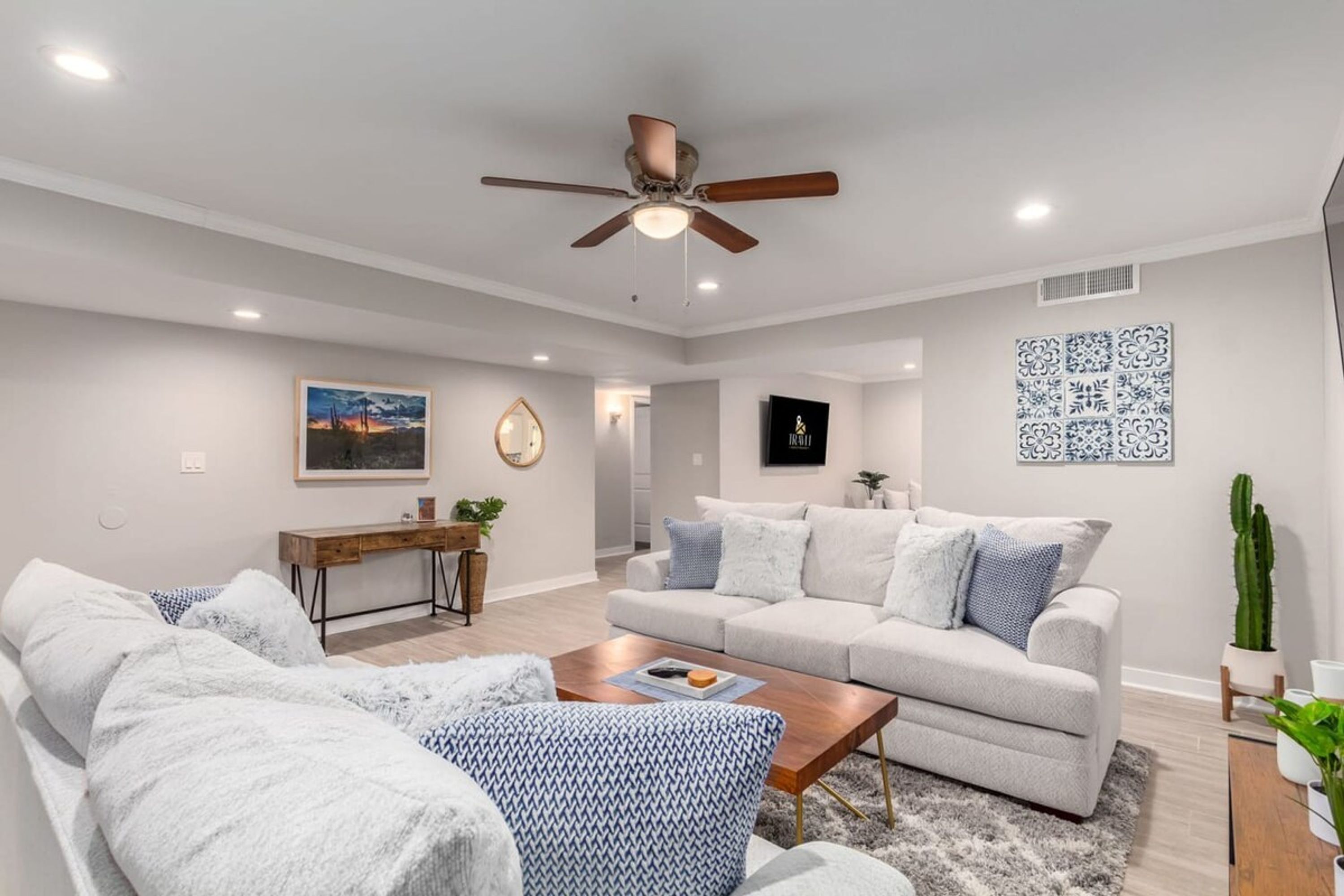 A spacious living room with a ceiling fan, a sofa set, a coffee table, and a dining area with a wooden table and chairs.