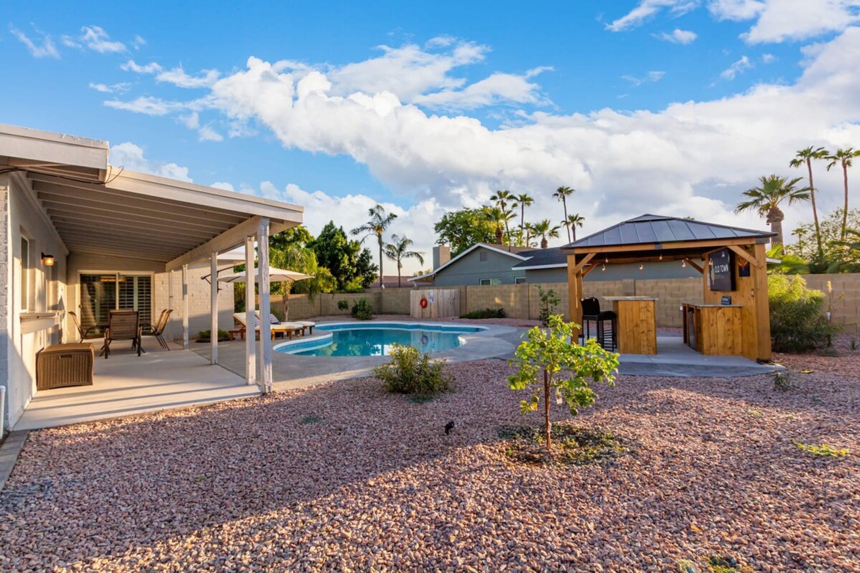 A backyard with a swimming pool, covered patio, and outdoor seating area.
