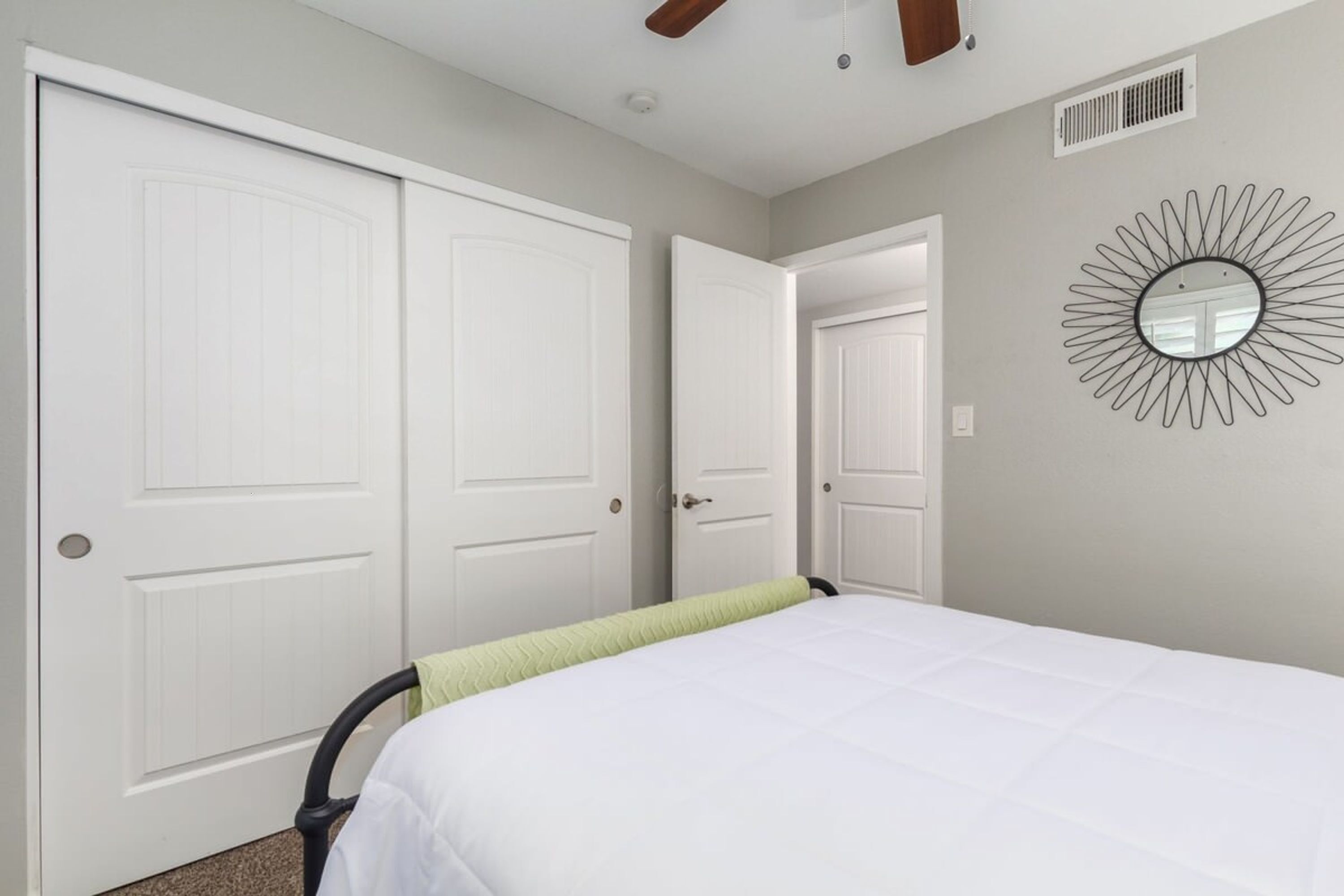 A bedroom with a bed, two white doors, a ceiling fan, and a wall-mounted mirror.