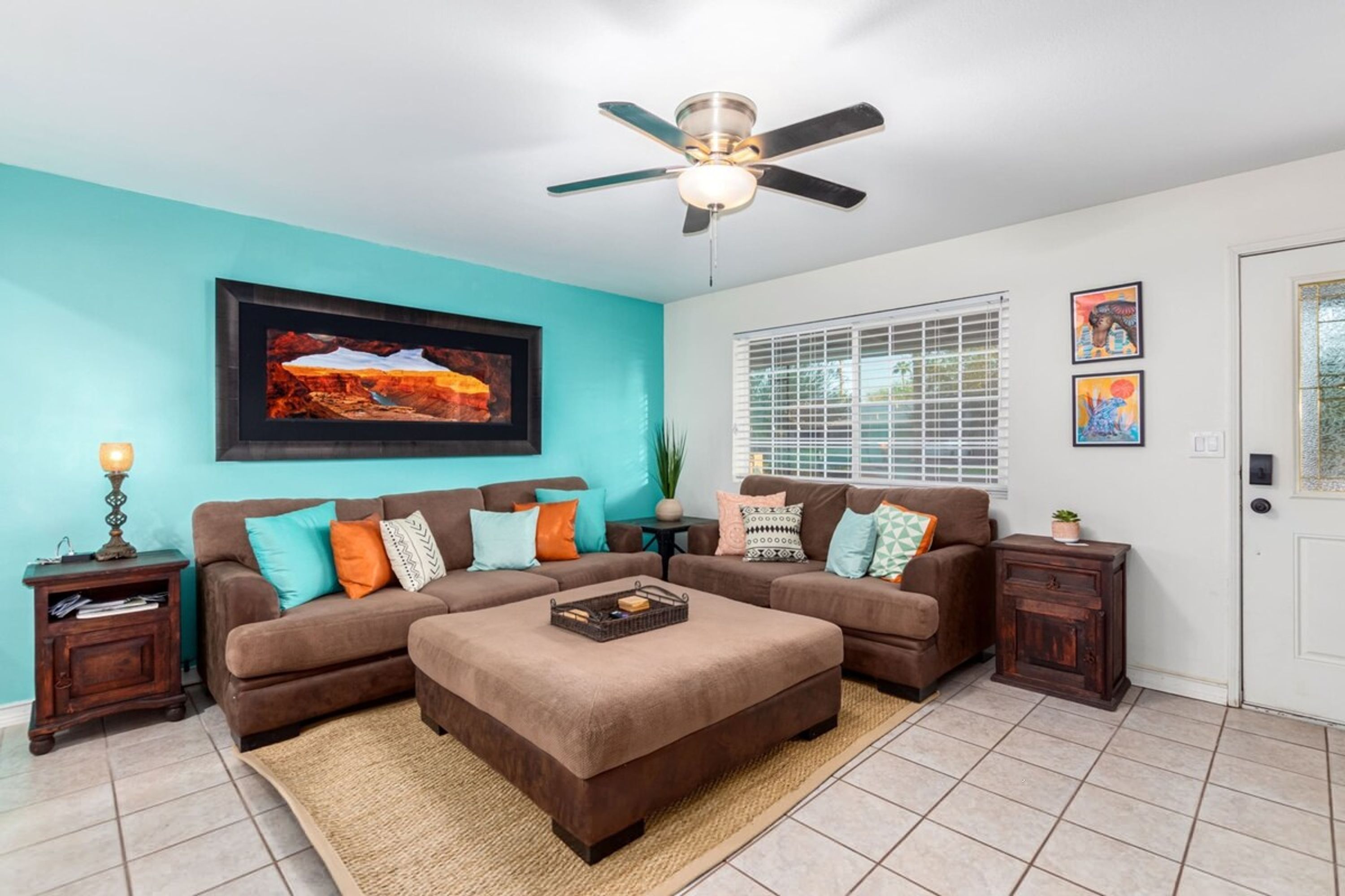 A living room with a sectional sofa, a coffee table, a ceiling fan, and a large window with blinds.