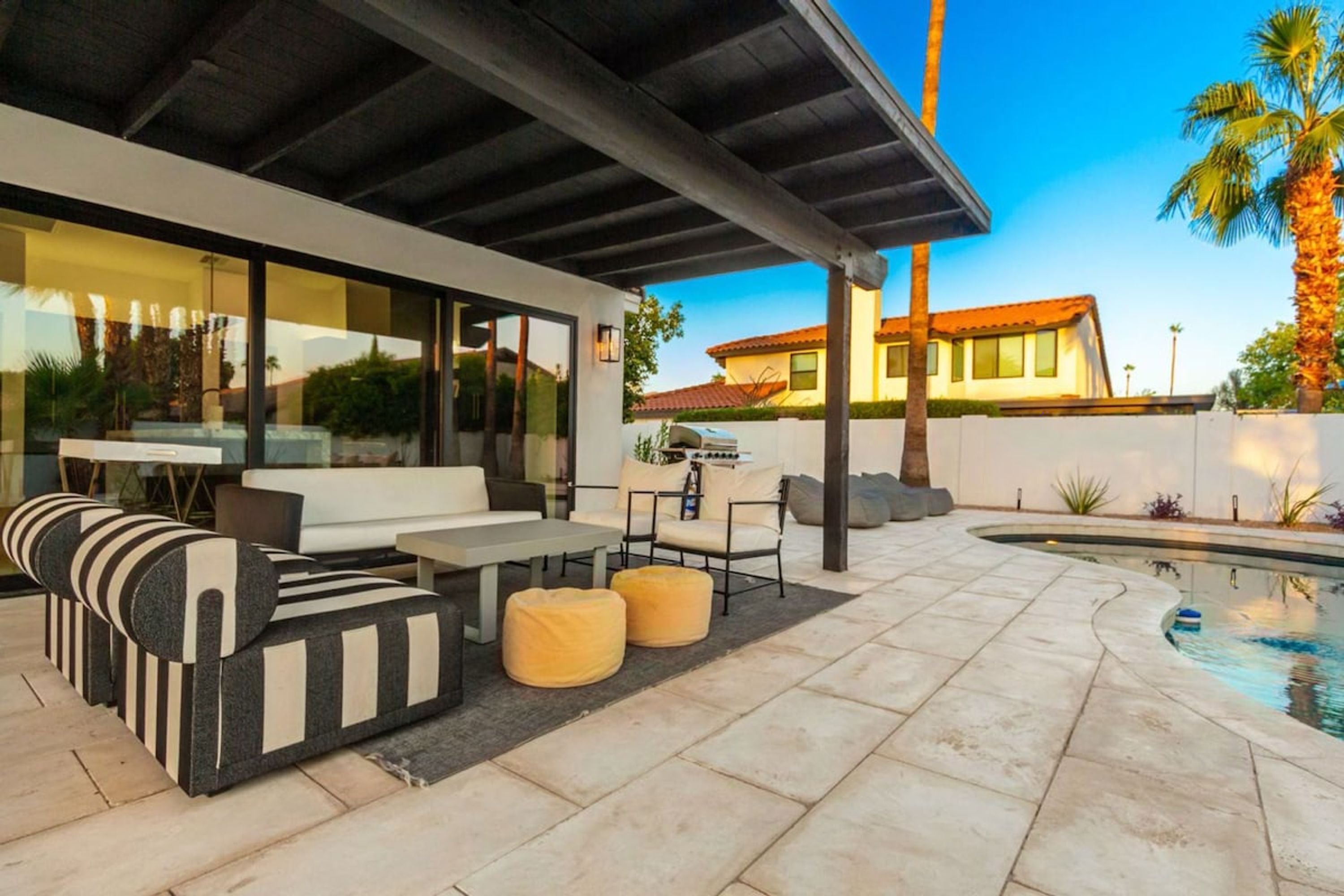 A modern outdoor patio with a pool, seating area, and a covered section.