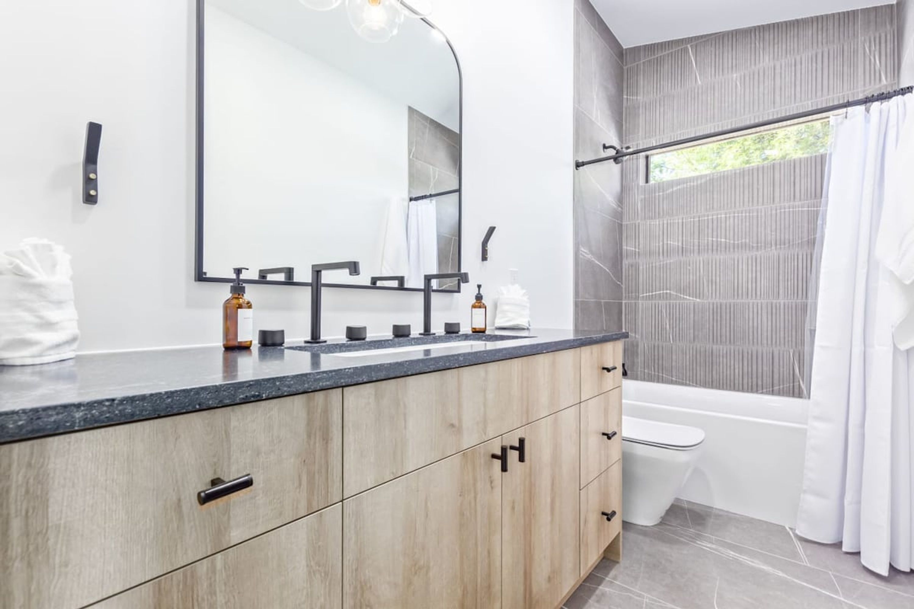 A modern bathroom with a wooden vanity, a large mirror, a bathtub, and a shower curtain.