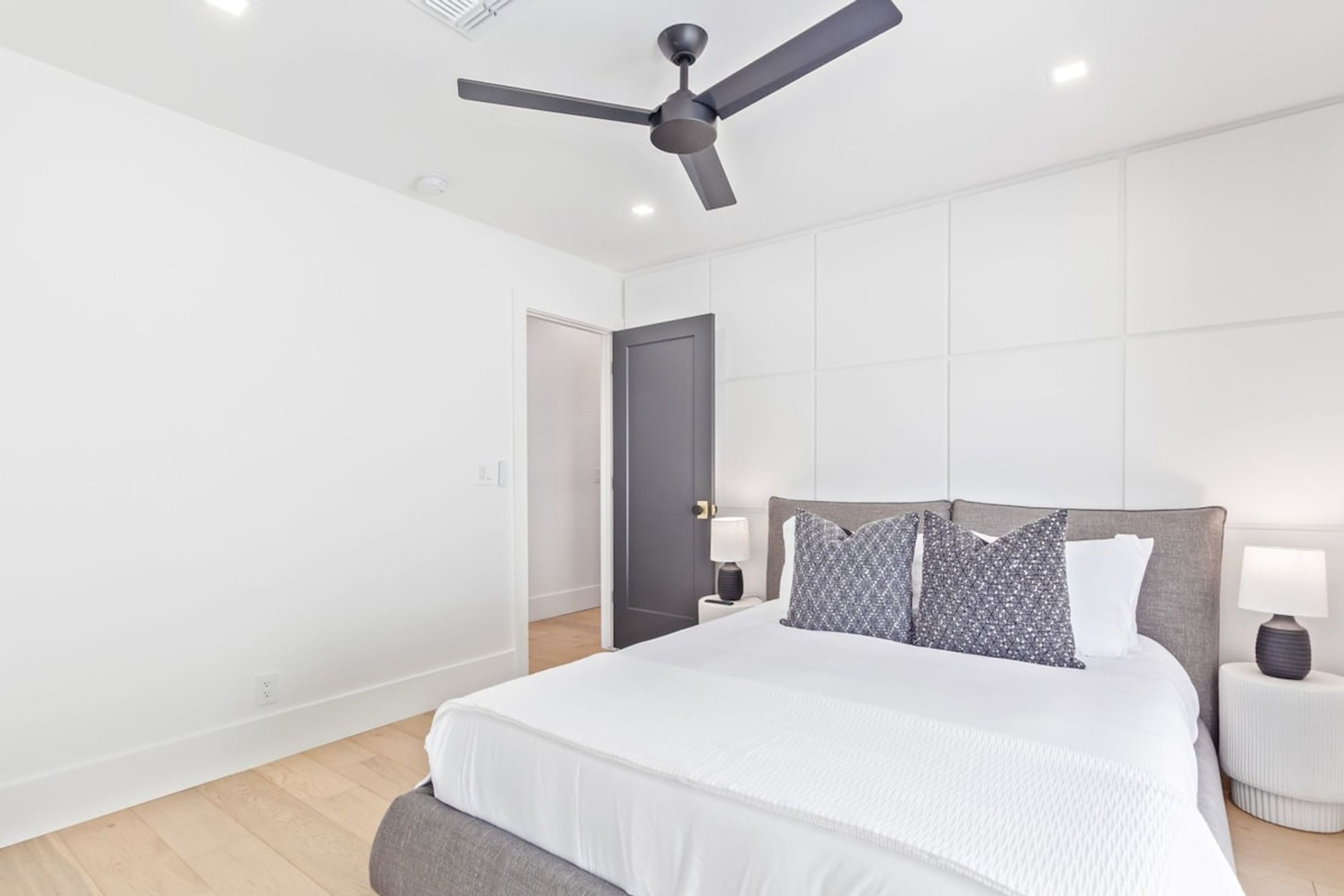 A modern bedroom with a large bed, a ceiling fan, and a nightstand with a lamp.