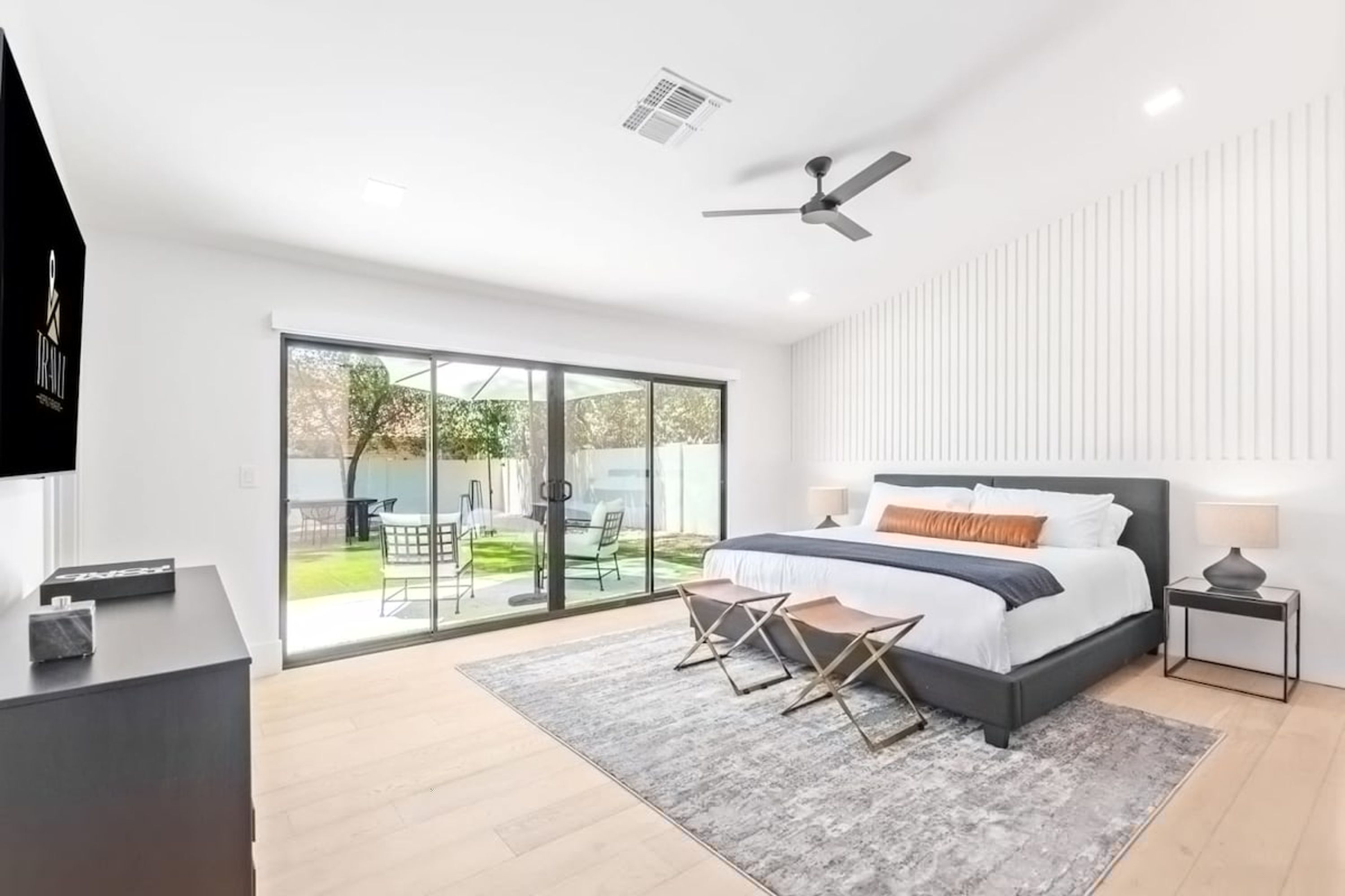 A modern bedroom with a large bed, a ceiling fan, and a sliding glass door leading to a patio.