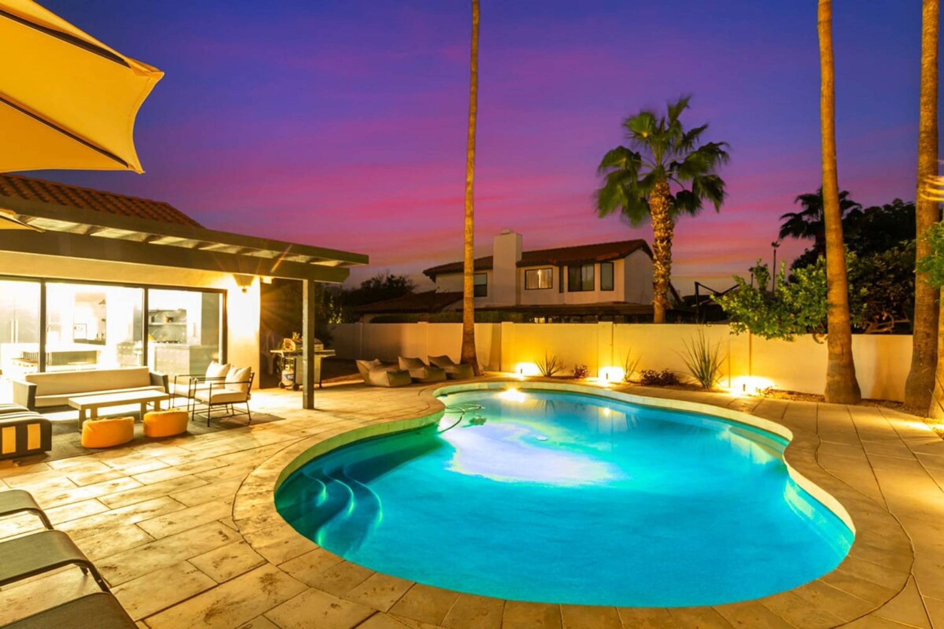Une piscine à bord incurvé, entourée d’un patio aménagé avec des meubles d’extérieur et un espace salon abrité.
