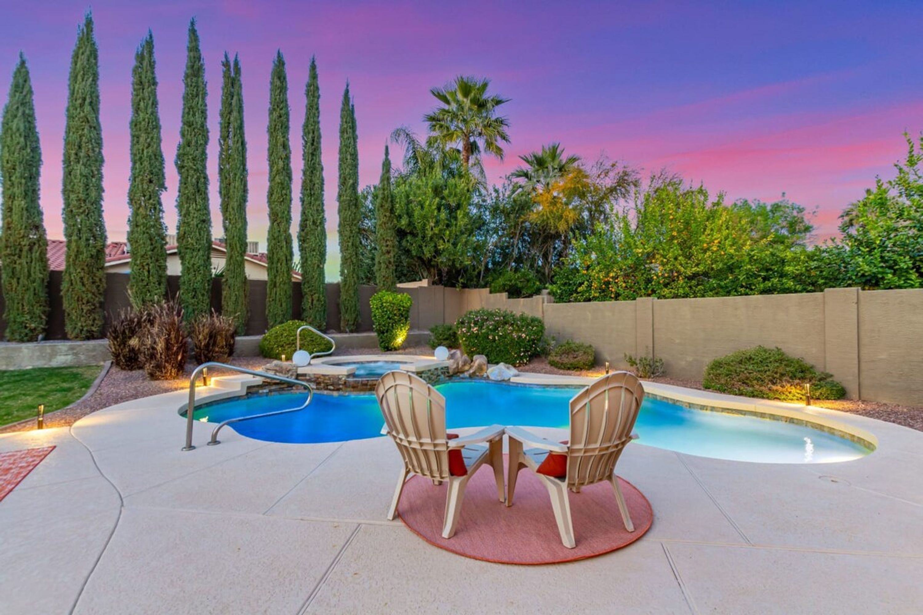 A backyard with a swimming pool, two chairs, and tall trees.