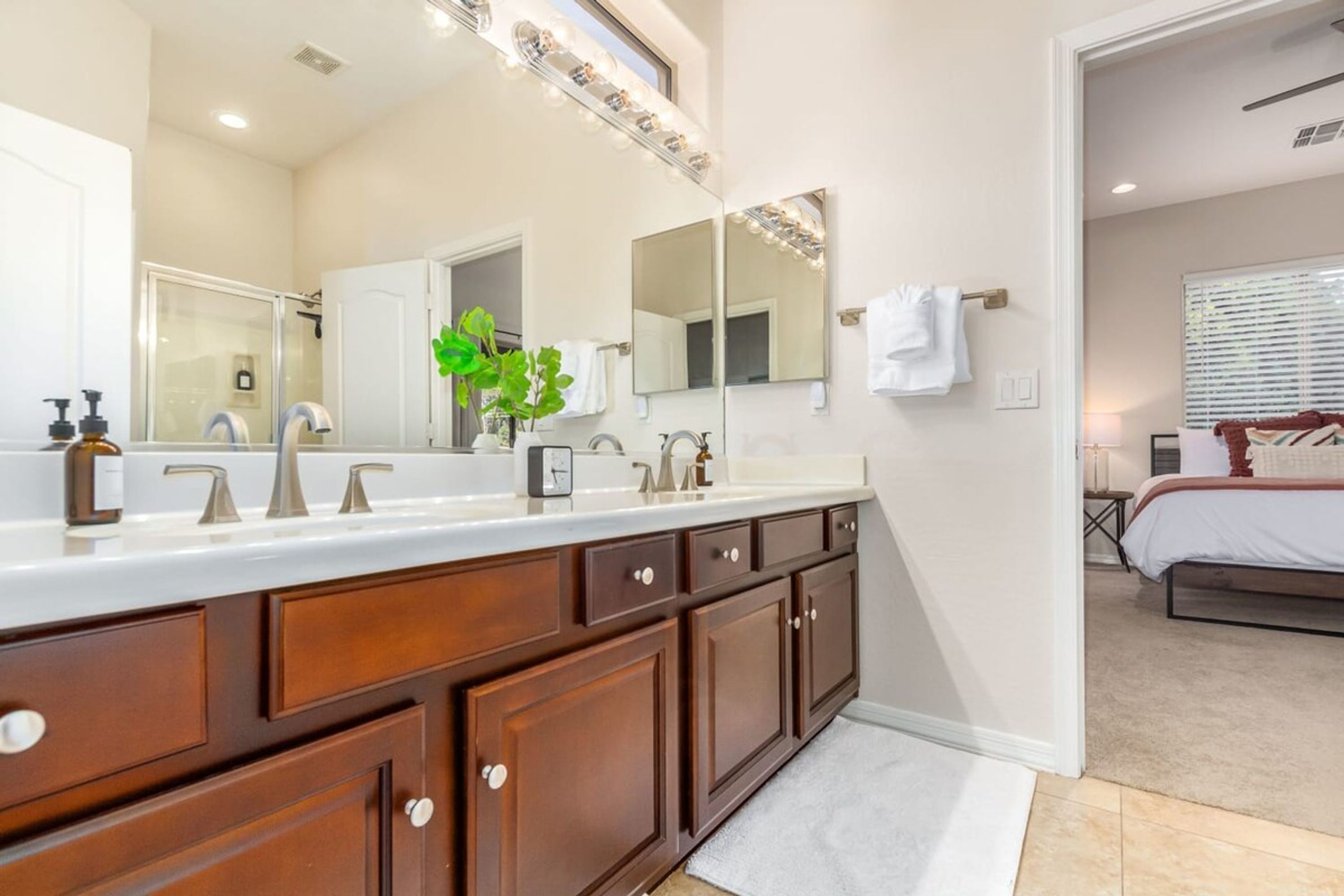 A modern bathroom with a large vanity, a mirror with lights, and a shower area.