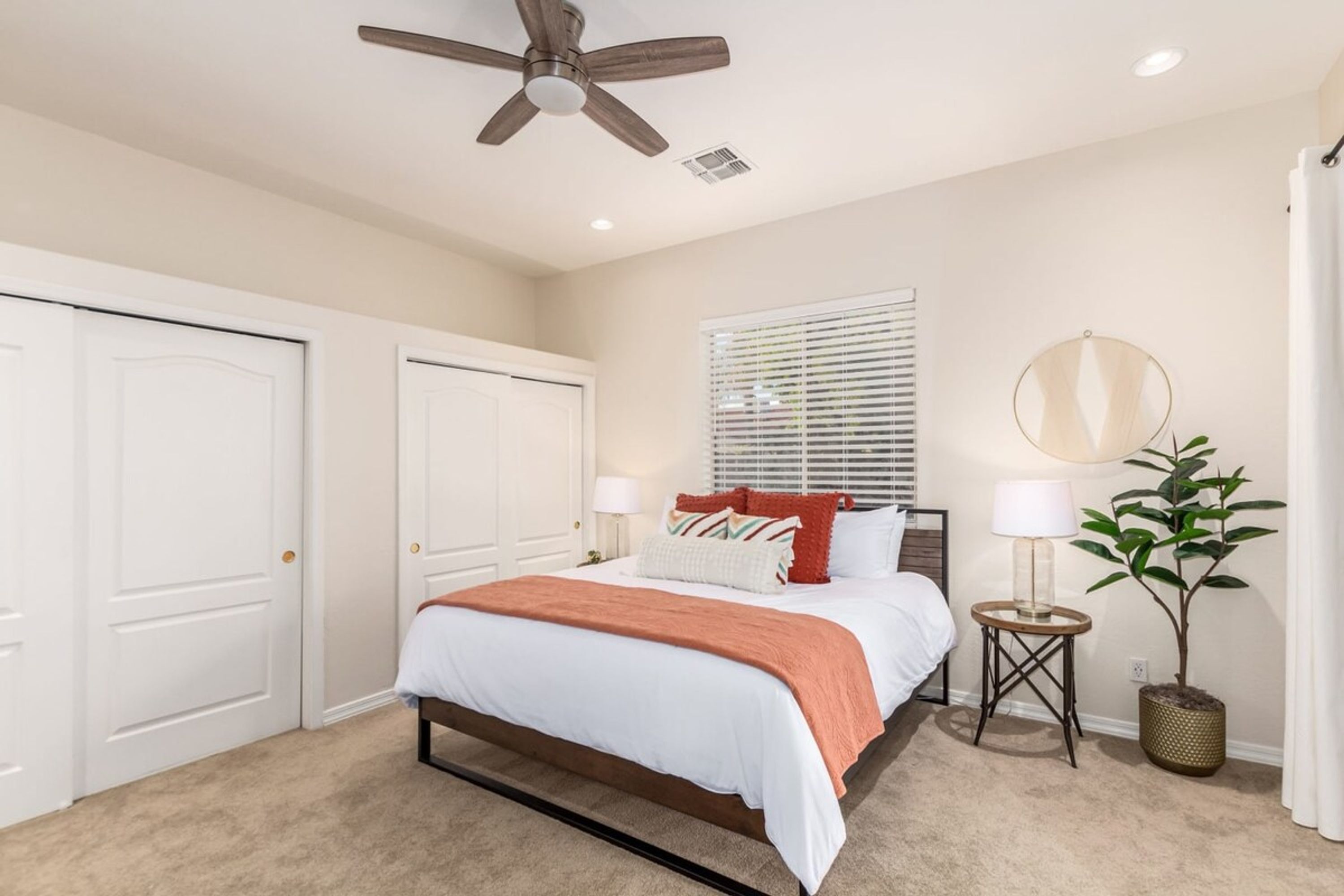 A bedroom with a bed, bedside tables, a ceiling fan, and a window with blinds.