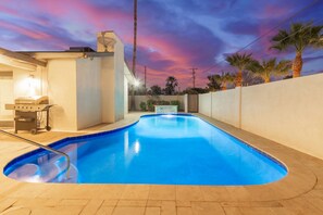 A swimming pool with a curved edge, surrounded by a tiled deck and a low wall.