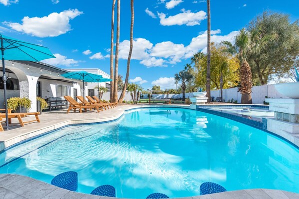 A swimming pool with lounge chairs and umbrellas, surrounded by palm trees and a clear blue sky. - Scottsdale Palms Pickle-putt-swim-bocce Bbq-gym (Scottsdale)