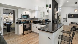 Una cocina moderna con muebles blancos, una isla central y un comedor con taburetes de bar.