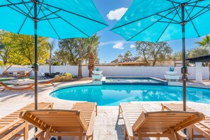 A pool area with wooden lounge chairs and blue umbrellas, surrounded by a white fence and palm trees. - Scottsdale Palms Pickle-putt-swim-bocce Bbq-gym (Scottsdale)