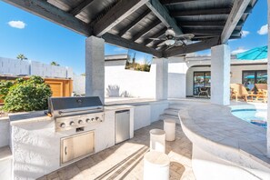 An outdoor kitchen with a grill, built-in oven, and a dishwasher, surrounded by a pool and patio furniture. - Scottsdale Palms Pickle-putt-swim-bocce Bbq-gym (Scottsdale)