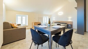 Un salon moderne et bien éclairé, comprenant un coin repas, un canapé et une table mise pour deux personnes.