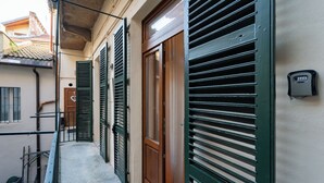 A narrow corridor with green shutters, a wooden door, and a small outdoor area with a metal railing. - La Dimora di Filippo (Cuneo)