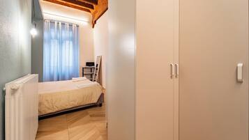 Ein Schlafzimmer mit einem Bett, einem Heizkörper, einer Holzbalkendecke, einem Kleiderschrank und einem Fenster mit Vorhängen.