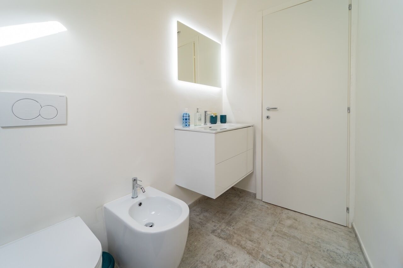 Une salle de bain moderne avec un lavabo blanc, un bidet et un miroir au-dessus du lavabo.