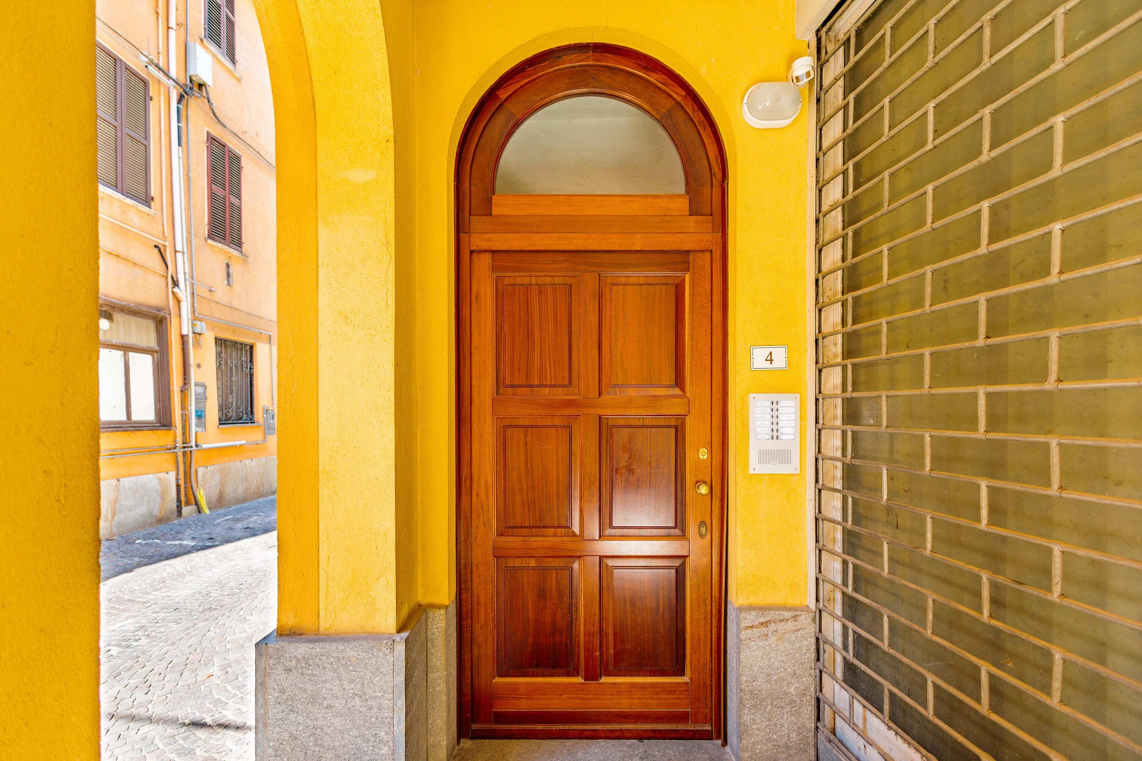 Uma porta de madeira com um painel de vidro, em um prédio amarelo com uma parede de tijolos à direita.