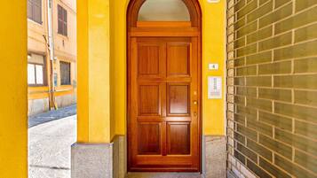 Uma porta de madeira com um painel de vidro, em um prédio amarelo com uma parede de tijolos à direita.