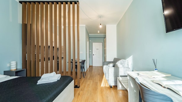 Una habitación de hotel moderna con cama, escritorio, silla, armario y televisor en la pared.