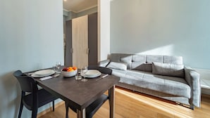 Una sala de estar moderna con un sofá gris, una mesa de comedor con platos y un cuenco de fruta, y piso de madera.