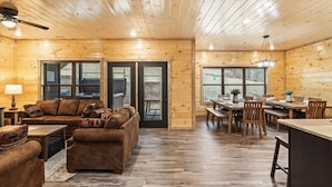 A spacious living area with a wooden ceiling, a sofa set, a dining table with chairs, and a kitchen area.