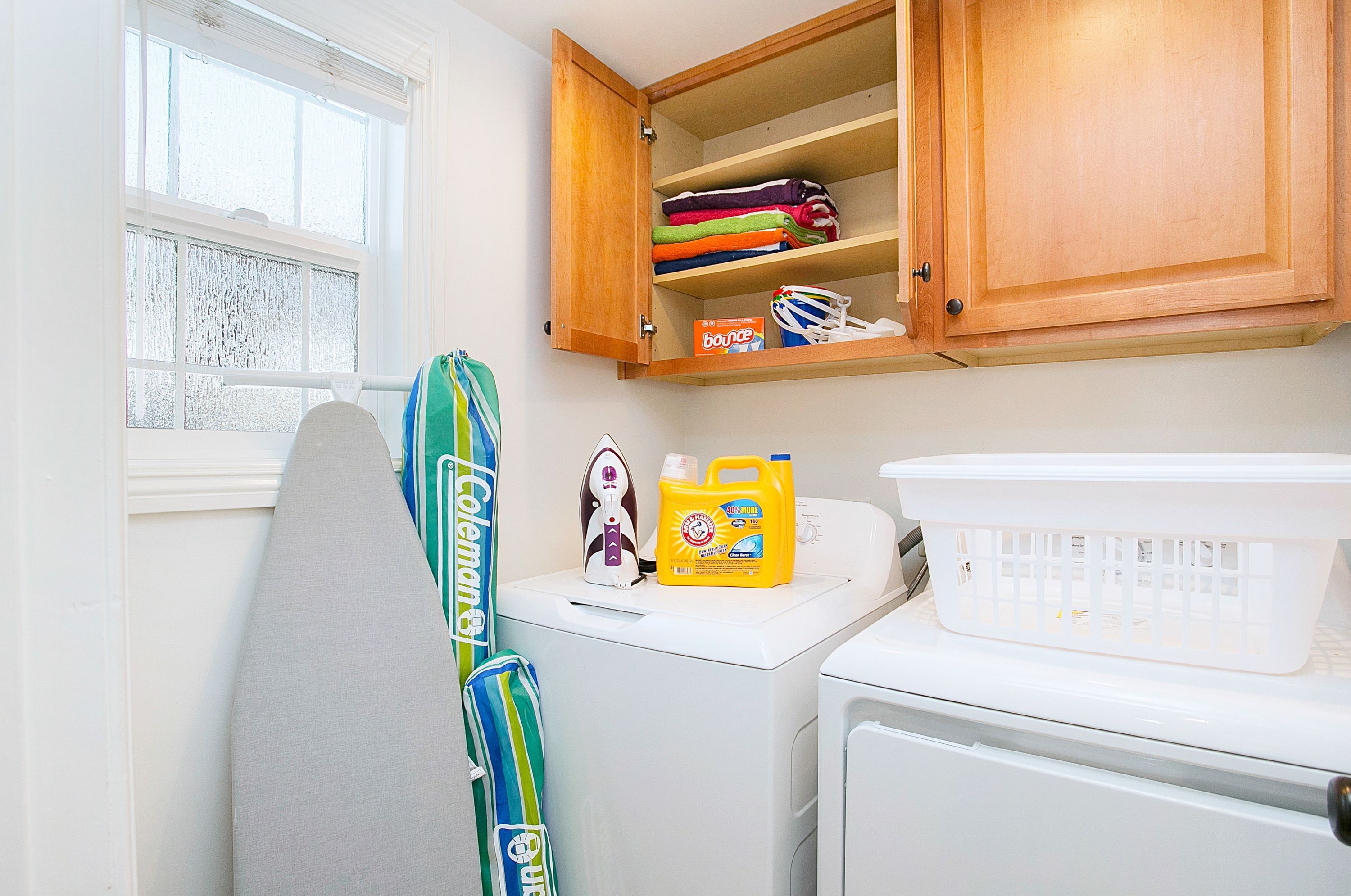 A laundry area with a washing machine, a drying rack, a wooden cabinet with folded clothes, and a laundry detergent bottle.