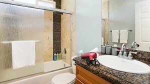 Un baño con cabina de ducha de vidrio, inodoro blanco, lavamanos con encimera de granito y espejo sobre el lavamanos.