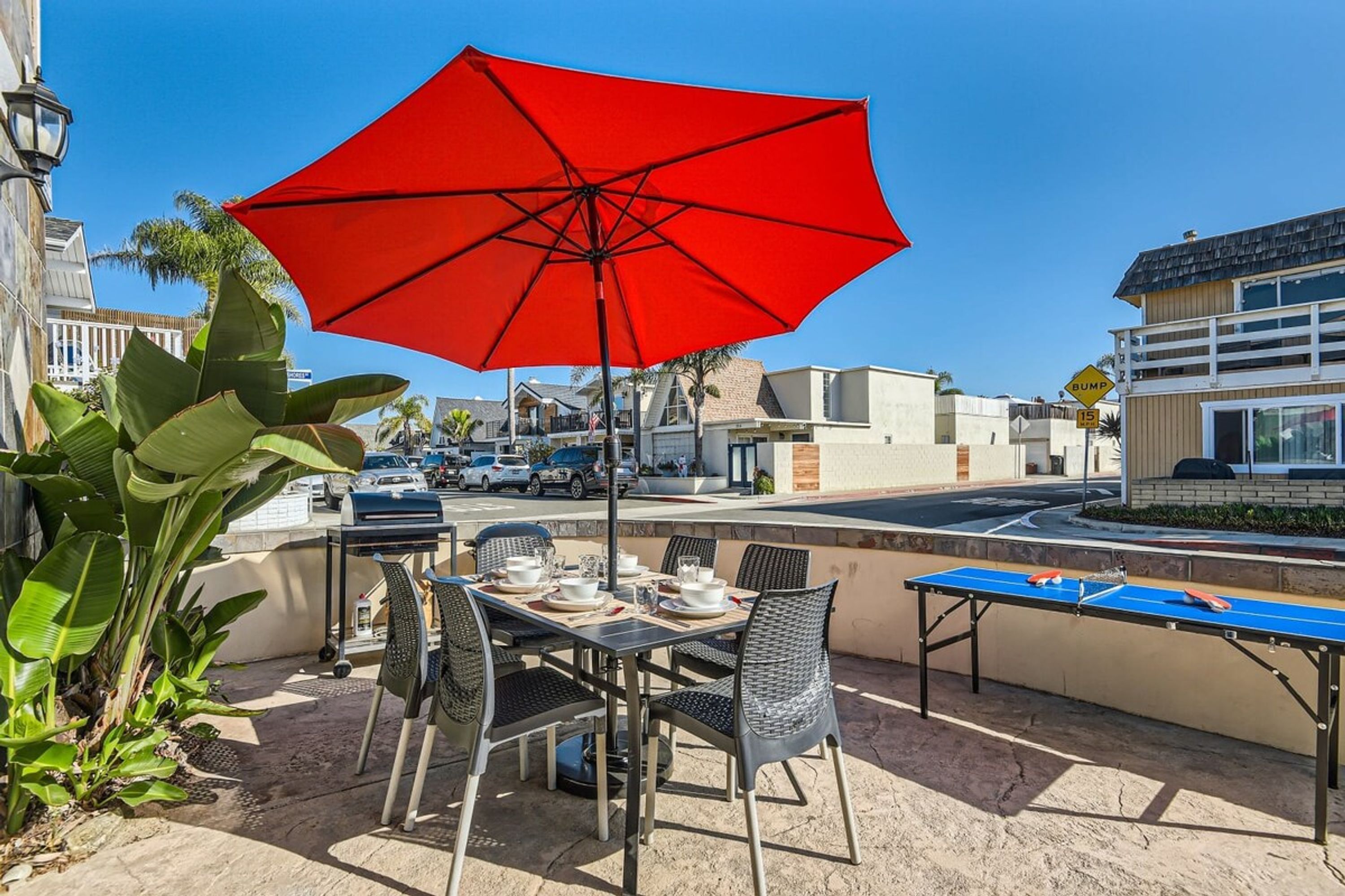 Un patio al aire libre con una mesa lista para comer, un paraguas rojo y una mesa de ping pong.