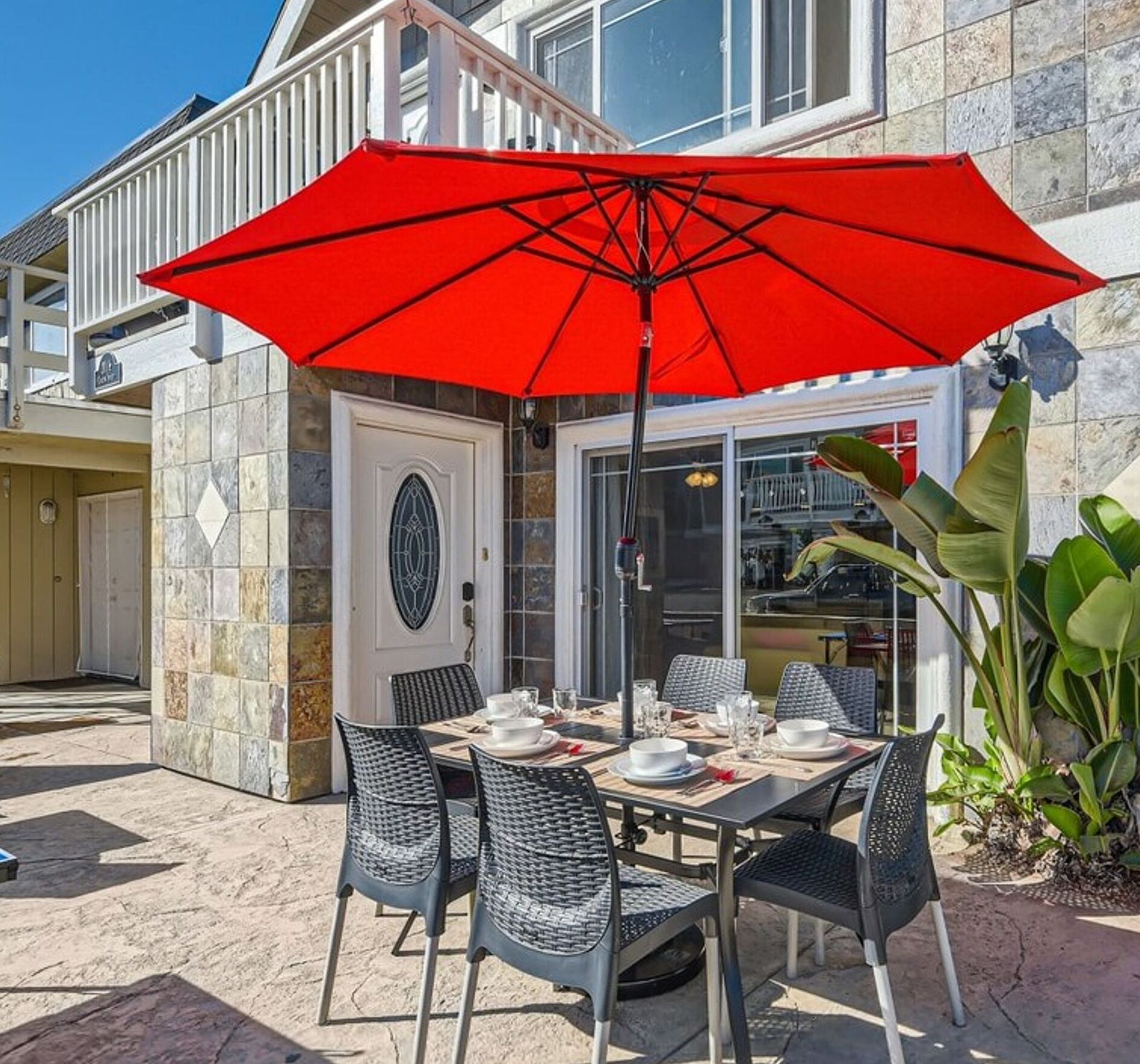 An outdoor dining area with a red umbrella, stone-tiled walls, and outdoor furniture.