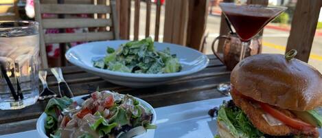 A table with a salad, a burger, a martini glass, and a water glass.