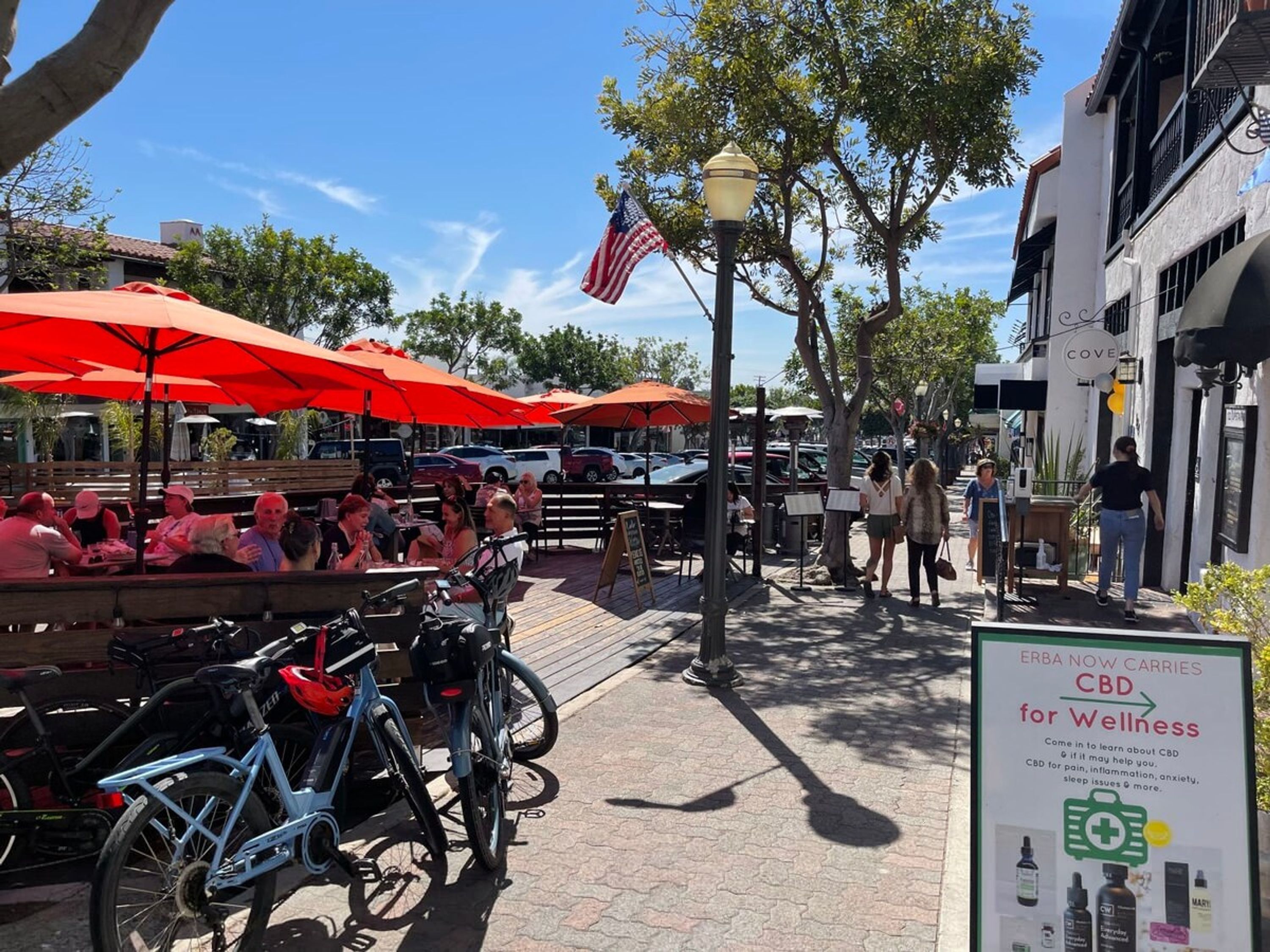 An outdoor cafe with red umbrellas, bicycles, and a sign advertising CBD for wellness.