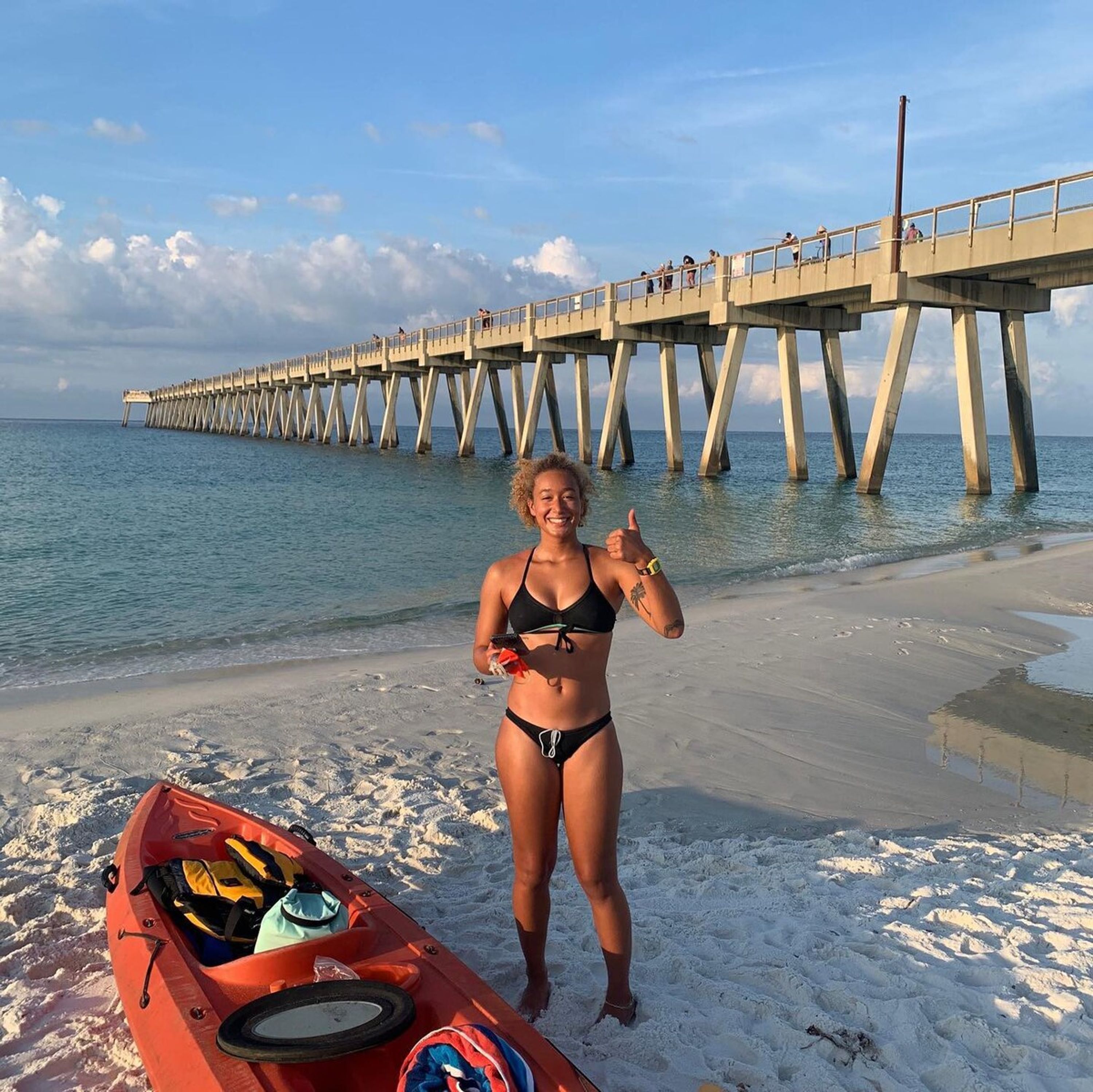 A beach with a kayak and a pier in the background.
