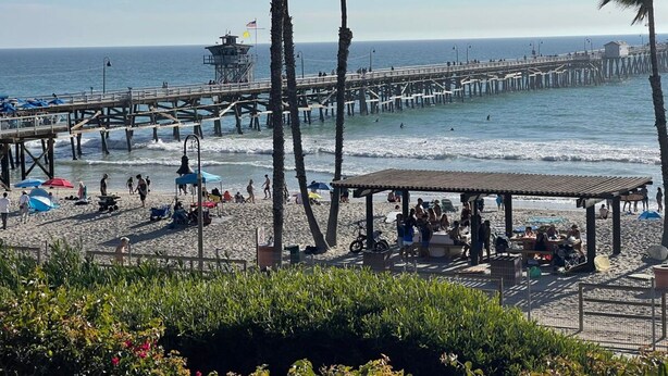 A beach with a wooden pier, palm trees, and beach umbrellas. - Walk to Beach - King Apt In 1 Area - AB (San Clemente)