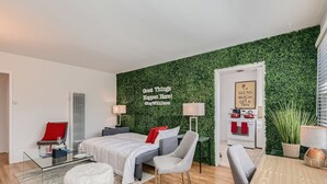 A modern hotel room with a green wall, a bed, a desk, a chair, a small table, and a lamp. - Walk to Beach - King Apt In 1 Area - AB (San Clemente)
