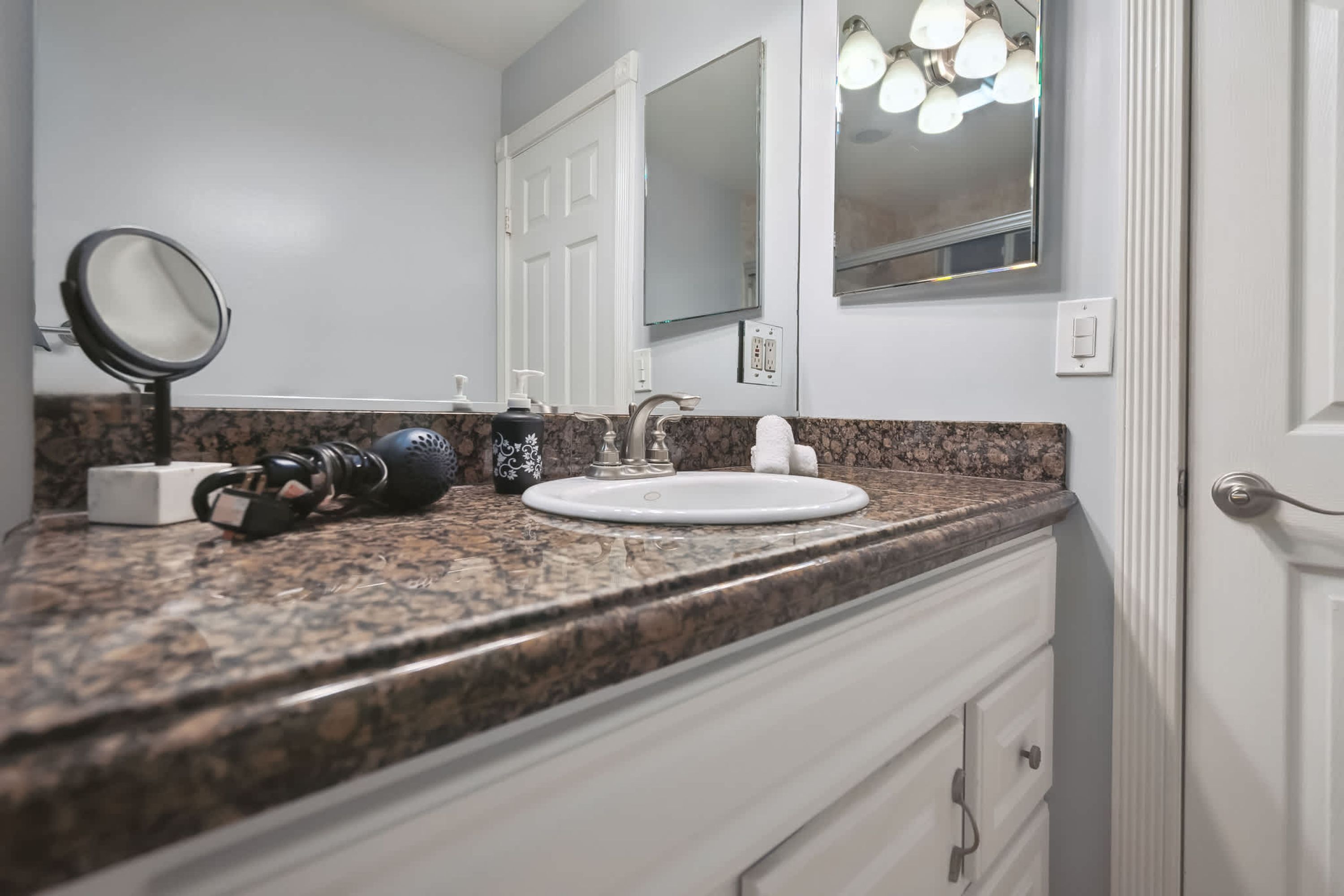 A bathroom with a granite countertop, a white sink, a round mirror, and a towel hanging on the wall.