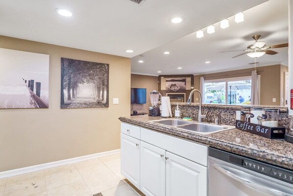 A modern kitchen with white cabinets, granite countertops, a coffee bar, and artwork on the walls. - Waking up in Your own 3BR Beach Home (Newport Beach)