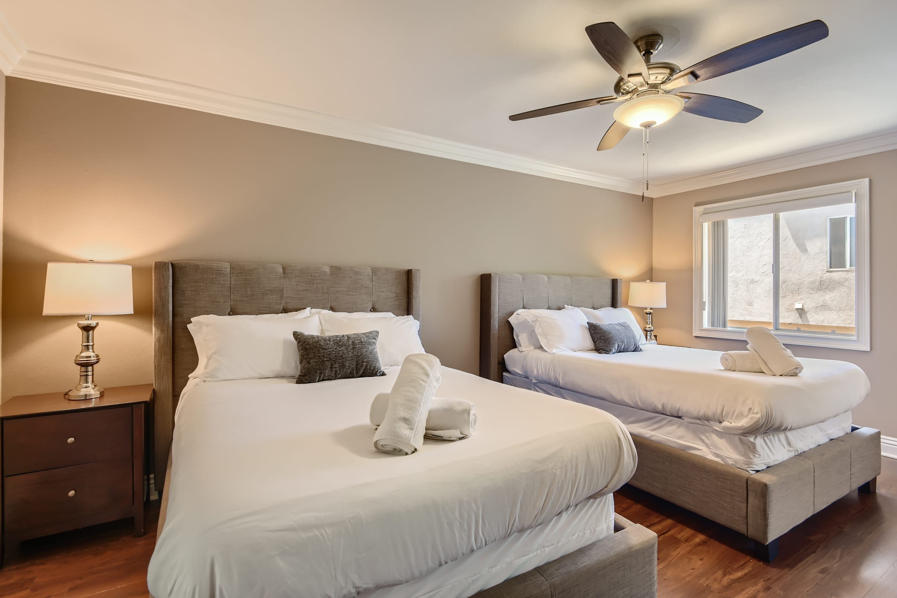 Une chambre d’hôtel avec deux lits, un ventilateur de plafond, des lampes de chevet et une fenêtre donnant sur un beau paysage.
