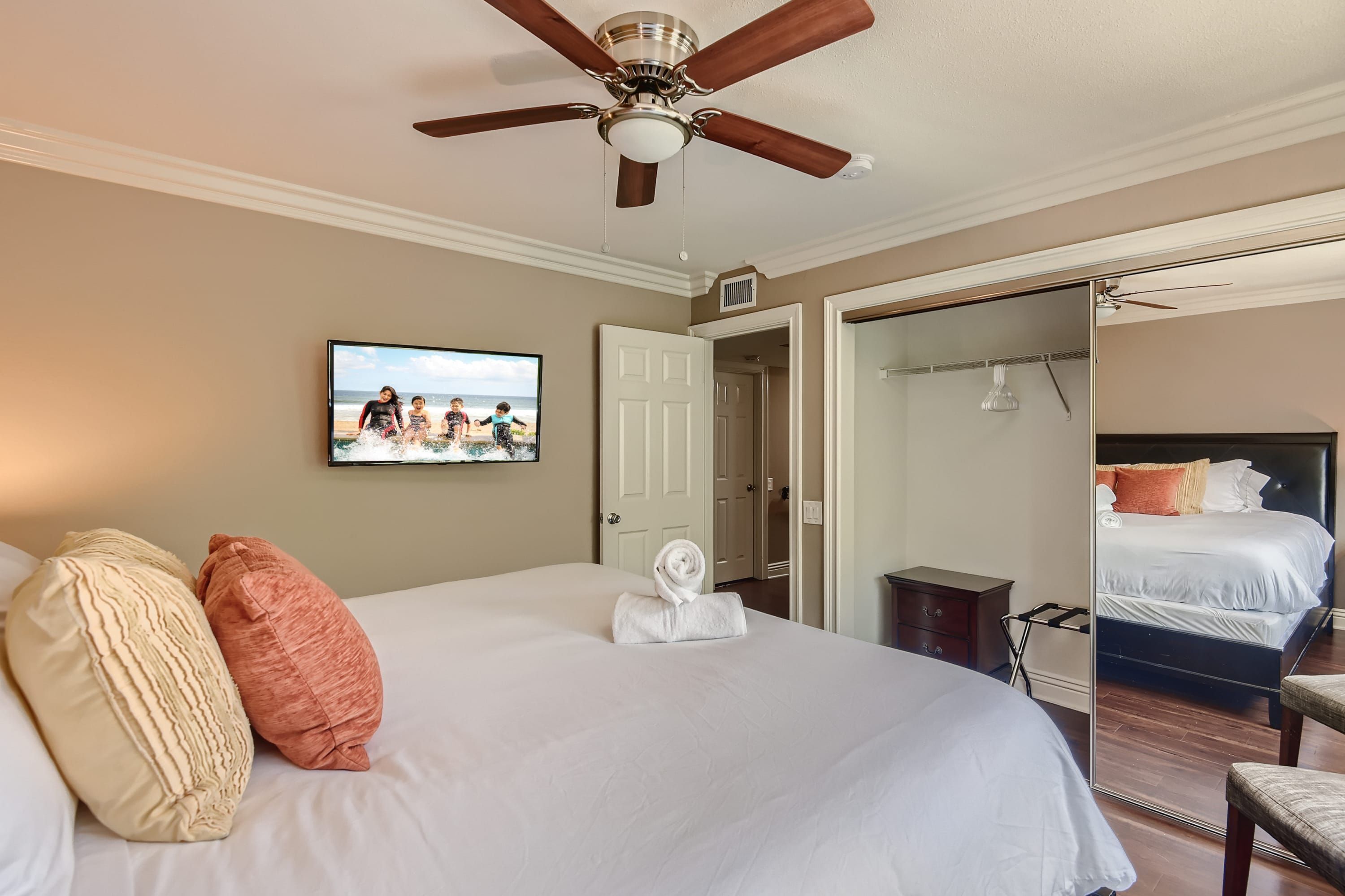 Habitación de hotel con una cama grande, ventilador de techo, televisor y espejo.