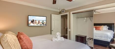 Habitación de hotel con una cama grande, ventilador de techo, televisor y espejo.