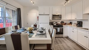 Une cuisine moderne avec des armoires blanches, des appareils en acier inoxydable et un coin repas avec une table dressée pour quatre personnes.