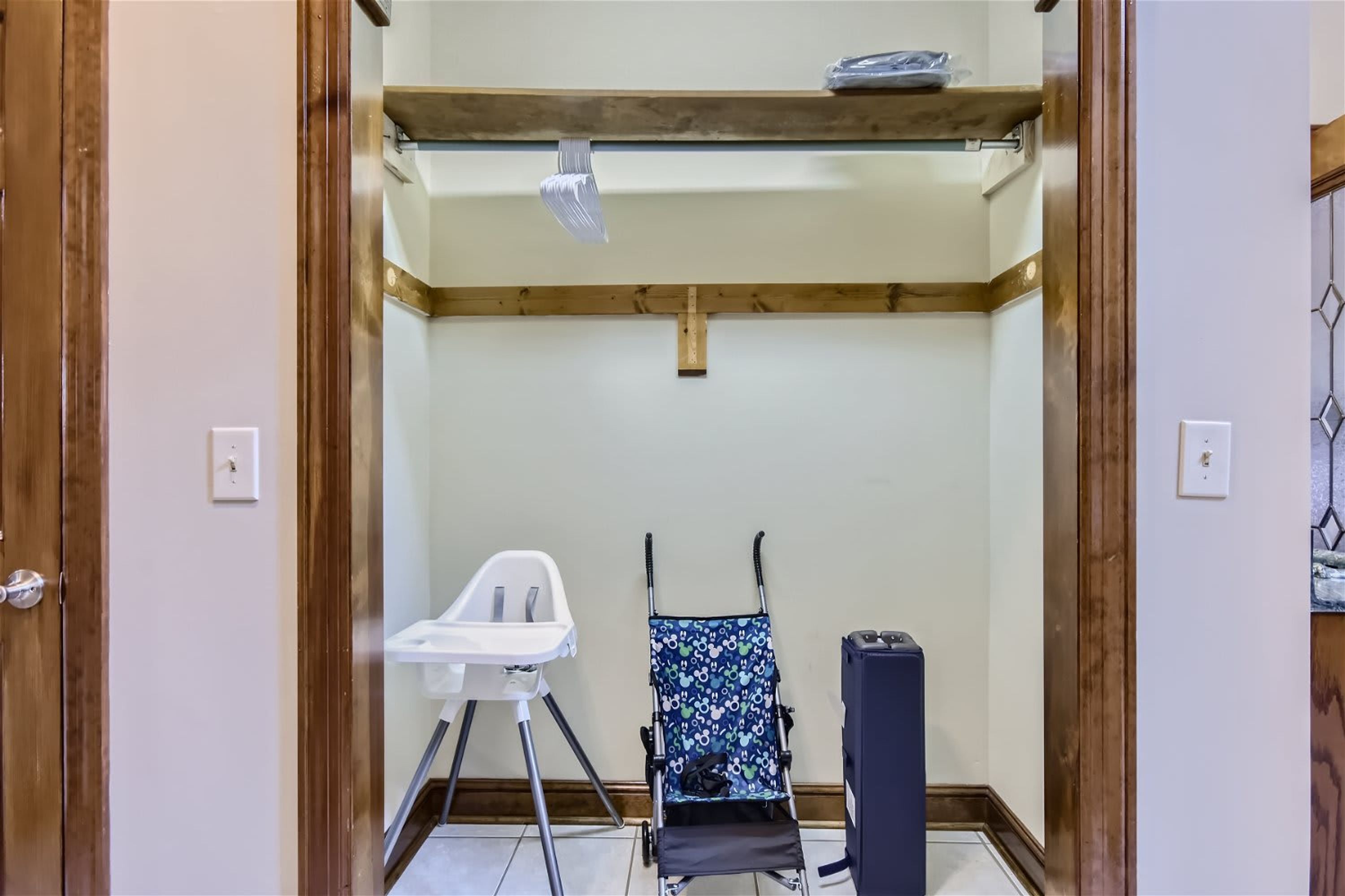Una habitación con techo de madera, una silla blanca, un cochecito de bebé y un cubo de basura.